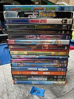 Stack of 19 kids DVD movies showing titles like Monsters vs Aliens, Pokémon Legends, Chicken Little, Frankenweenie, Legend of the Guardians, Shrek, Ice Age, Finding Nemo, The Lorax, Ratatouille and Bango.