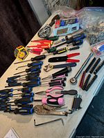 Photo showing various hand tools including screwdrivers with blue and pink handles, locking pliers, adjustable wrench, ratchet, and some hardware items on a table.