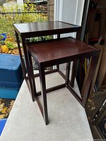 Two dark wood nesting tables positioned outside showing size difference.