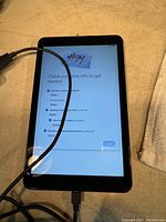Samsung Galaxy tablet powered on, displaying setup screen, connected to charging cable, on a surface next to a cloth.