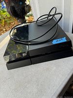 Sony PS4 console with power cable shown outside on a surface with a background of a door and outdoor surroundings.