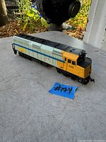 Side view of vintage VIA locomotive model 6410 placed on a surface outdoors, showing yellow, blue, and gray paint with Canadian flag and VIA logo.