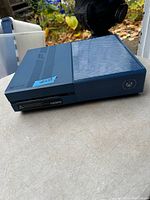 Blue Xbox console on a table, front view showing disc drive and Xbox logo