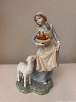 Front view of the ceramic figurine showing the girl holding a basket and the sheep standing beside her