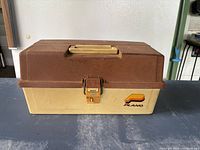 Closed brown and beige vintage Plano fishing tackle box with a latch and handle.