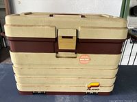 Front view of the vintage Plano tackle box showing beige and brown plastic, latch, handle, and Plano logo at the bottom right corner.
