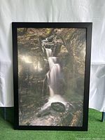 Front view of photographic print depicting a waterfall scene in a black frame.