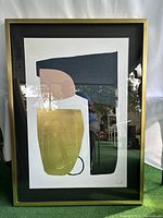 Front view of framed abstract wall art with geometric shapes in navy, pink, green, and black inside a gold metal frame.