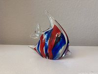 Side view of colorful glass fish paperweight showing red, blue, and black swirls inside clear glass body with sculpted fins.