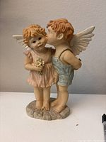 Front view of pair of kid angel resin figurines showing boy kissing girl on cheek with girl holding flowers.