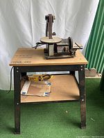 Full view of the Dremel 1731 disc and belt sander mounted on Craftsman metal table with shelf holding sanding belts and sandpaper.