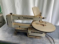 Side view of Dremel 16-inch scroll saw showing frame, worktable, and blade holder with rust and sawdust.