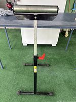 Front view of a metal roller stand with two leg support, height adjustable vertical post with red lock.