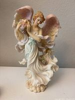 Front view of the Seraphim Classics vintage 1998 angel figurine showing pink and white wings, flowing robes, holding a cornucopia of grapes.