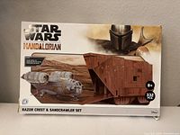 Front view of the box showing Star Wars The Mandalorian Razor Crest and Sandcrawler paper model kit with 332 pieces, age recommendation 8+.