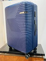 Front and right side view of blue hard-shell spinner suitcase with ridged chevron pattern and carry handles.