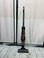 Full upright view of the red and black BISSELL cordless stick vacuum with long handle on carpet.