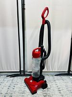 Front angled view of the red Dirt Devil Endura Compact upright vacuum cleaner showing the handle, hose, and dust cup with logo.