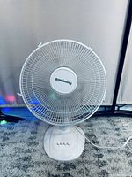 White Honeywell desk fan on carpeted floor, front view showing blade grill and base controls.