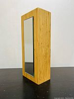 Front angle showing the bamboo wood block with mirror inset on one side standing upright on a black surface against a white wall.