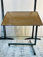 Front angled view of the modernist side table showing the angled wooden top with striped woodgrain and dark metal frame base on wheels.