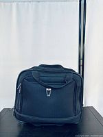 Front view of a black rolling bag showing zippered compartments and padded handles.
