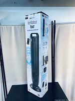 Photo of Dyson tower fan box with image of the fan and remote control on packaging. Black vertical tower fan shown in image. Box states features and shows branding.