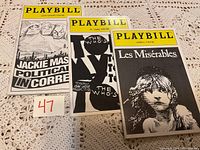 Three Playbill theatre programs on a crocheted surface showing Jackie Mason's Political Incorrect, The Who's Tommy, and Les Misérables.