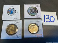 Four coins in white cardboard holders: Ohio quarter, Pearl Harbor half dollar, 2000 $1 coin, 1981 Susan B. Anthony dollar