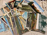 Array of colorful postcards showing various scenic views, buildings, and floral gardens spread loosely on a lace cloth surface.