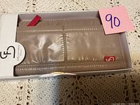 Top view of new beige/tan wallet in white Stella & Fritz packaging with red logo tag and fabric pull tab visible.