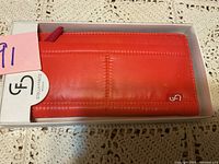 Photo of a red leather Stella & Fritz wallet in its original white branded box on a lace surface.