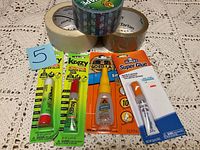 Photo of the set of adhesive products including super glues and rolls of tape on lace tablecloth.