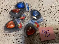 Five Refresh brand car air fresheners in sealed plastic packaging placed on a cream crochet background, showing the assorted colors of blue, red, and orange gels inside grey plastic triangular holders.