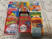 Photo showing all unopened baseball card packs from various brands arranged on a textured surface.