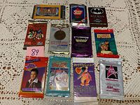 Twelve unopened packs of trading cards displayed on a lace tablecloth with variety of vintage themes and brands.