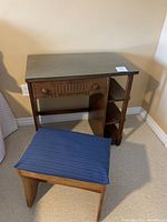 Oblique angle view of dark wood desk with glass top, drawer and shelves, and matching blue upholstered stool