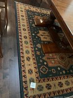 Photo showing the area rug under wooden dining table with visible geometric and floral pattern in hunter green, taupe and paprika colors.