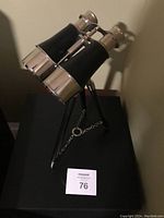 Side view of the nautical binoculars showing brass and black leather detailing on the barrels and tripod stand with chain support beneath.