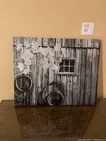 Full view of the canvas print leaning against a wall, showing the barn wall, window, leaves and wheels
