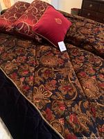 Comforter spread out showing chintz floral pattern and black velvet trim with gold piping, along with red decorative cushions.