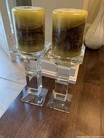 Front view of two crystal candle holders each holding a green and brown marbled wax candle.