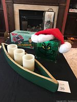 Photo showing green wooden canoe holding three flameless battery-operated candles, green glittery Grinch glass block doorstop with Santa hat, and original box for automatic card shuffler.