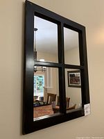 Front view of rectangular wall mirror with four glass panes and dark distressed wooden frame reflecting dining area