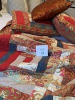 Red themed quilt spread showing detailed patchwork design with floral and paisley accents, and pillow shams on bed