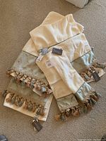 Set of six new Croscill Home designer towels with tags, cream colored with multi-colored tassels and satin borders