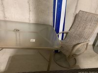 Photo of rectangular outdoor table with frosted glass top and one taupe swivel sling chair beside it against concrete wall