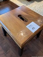 Photo showing top of Acacia wood stool with rectangular cut-out handle and lot number sticker.