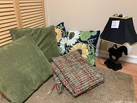 All items grouped showing the 4 pillows, multicoloured throw blanket, and horse table lamp on carpeted floor against closed wood slats.