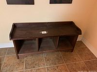 Dark solid wood bench front view showing three cubbies and raised back and side edges on the top surface.